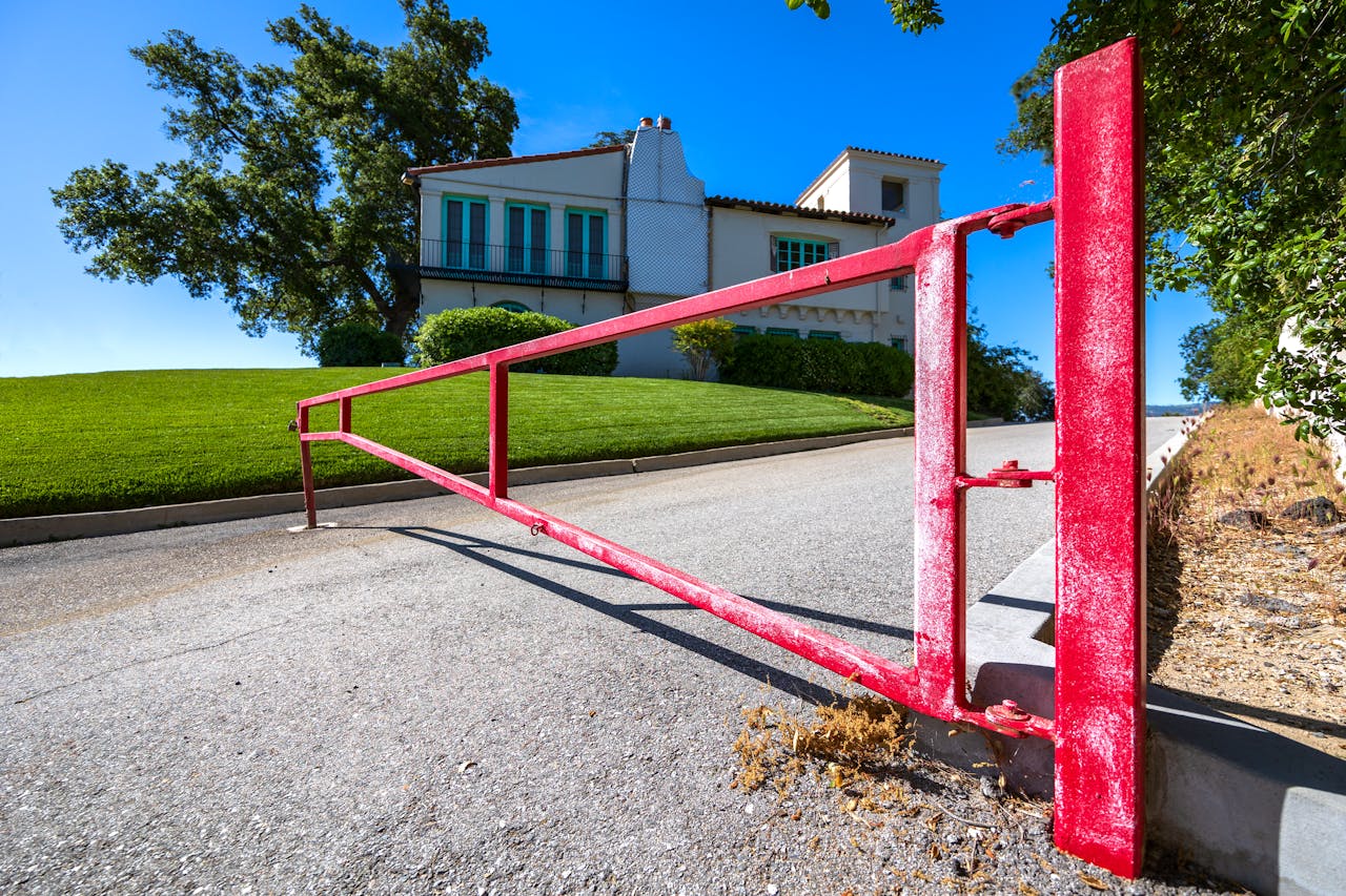 about-us A bold red gate on a sunny day, marking the entrance to a beautiful hillside residence.